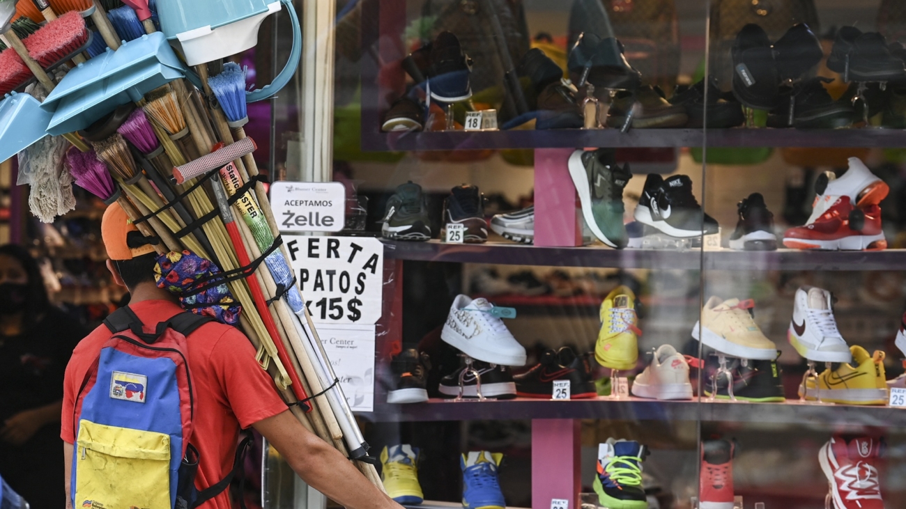 A vendor of brooms and cleaning implements observes the window of a shoe store that offers bargains in US dollars according to the new currency conversion in Caracas on October 1, 2021. The official exchange rate of the Venezuelan bolivar went from 4.18 million to the US dollar overnight to just 4.18 as the impoverished country slashed six zeroes off its inflation-battered currency Friday to simplify transactions. (Photo by Yuri CORTEZ / AFP)