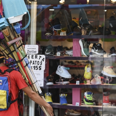 A vendor of brooms and cleaning implements observes the window of a shoe store that offers bargains in US dollars according to the new currency conversion in Caracas on October 1, 2021. The official exchange rate of the Venezuelan bolivar went from 4.18 million to the US dollar overnight to just 4.18 as the impoverished country slashed six zeroes off its inflation-battered currency Friday to simplify transactions. (Photo by Yuri CORTEZ / AFP)